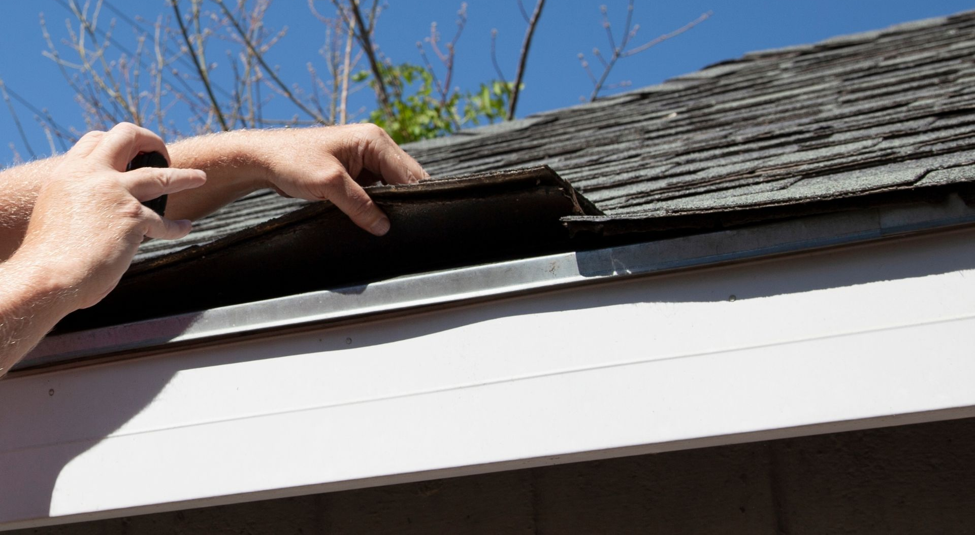 Worker lifting roof shingles to inspect a gap under the edge of a house roof