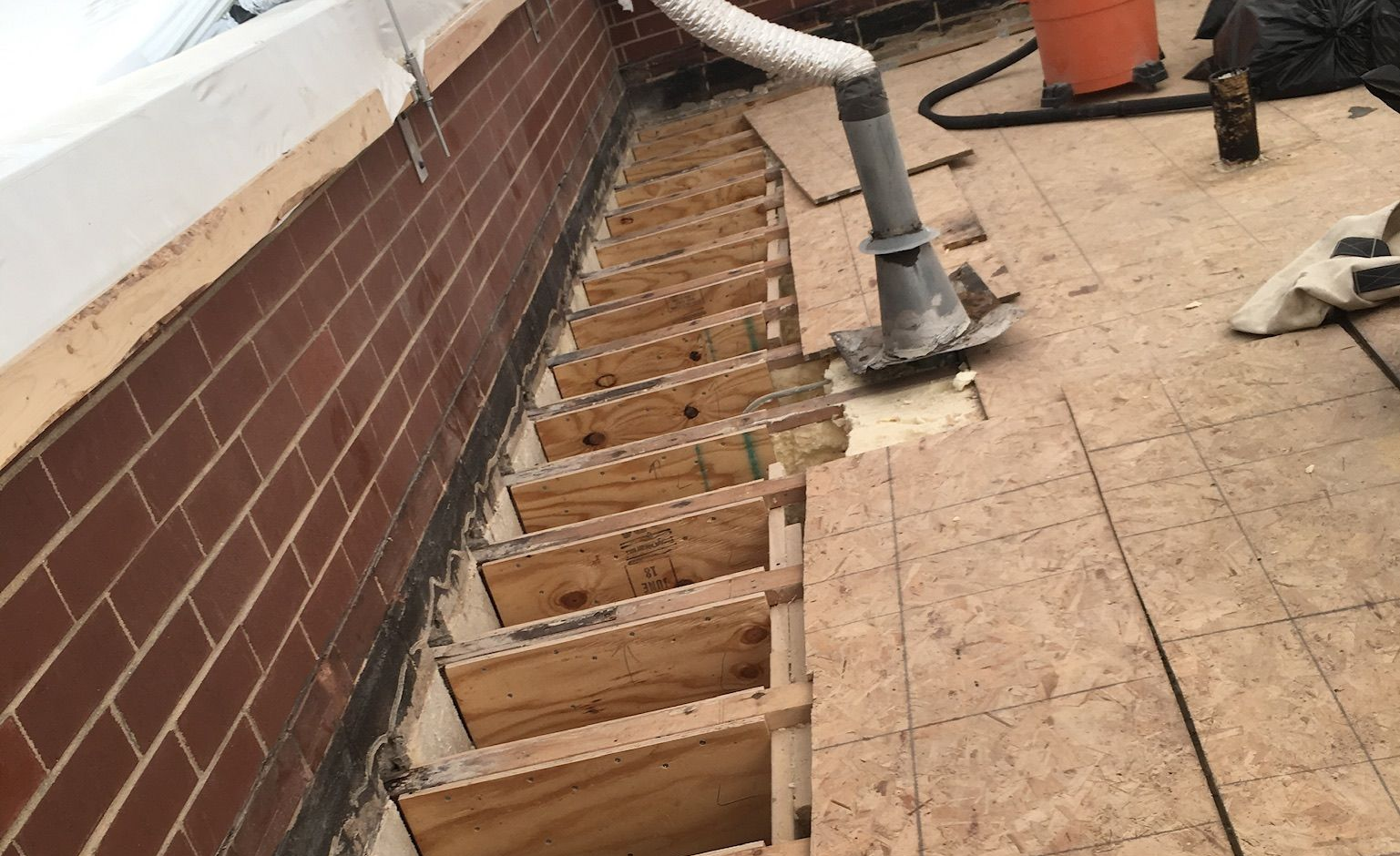 Exposed wooden floor joists and subfloor under repair beside a brick wall and roof edge
