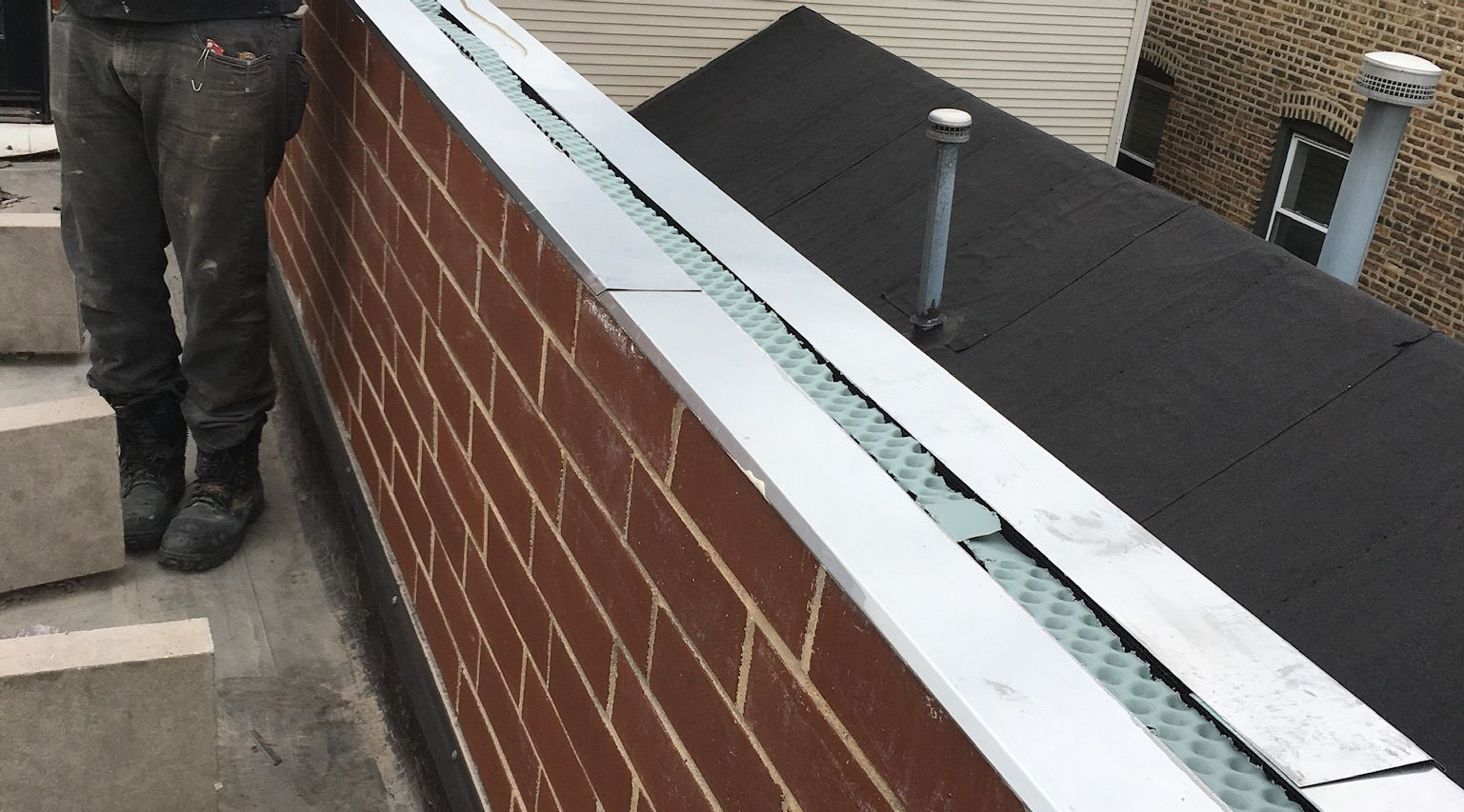 Worker standing beside a brick wall with flashing on top of it