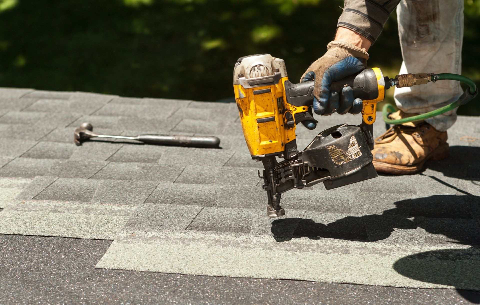 Worker using a yellow nail gun to install shingles on a roof