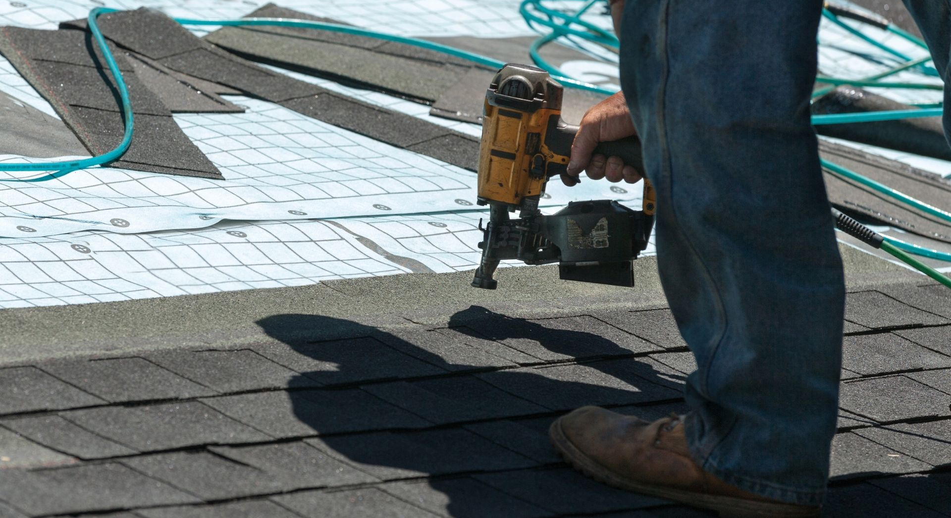 Worker using a nail gun to install shingles on a roof