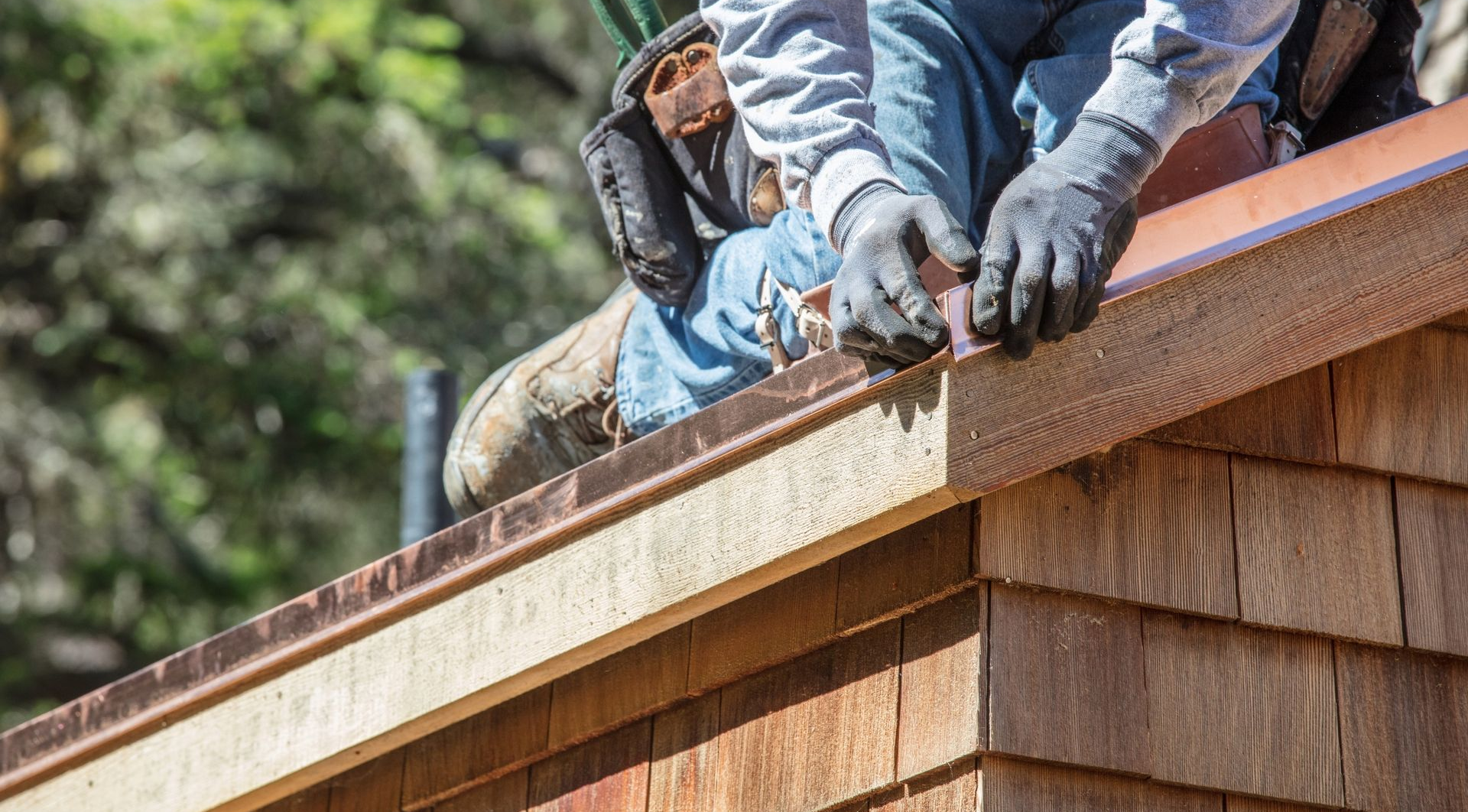 Worker installing brown copper flashing on edge of shingled sloped roof