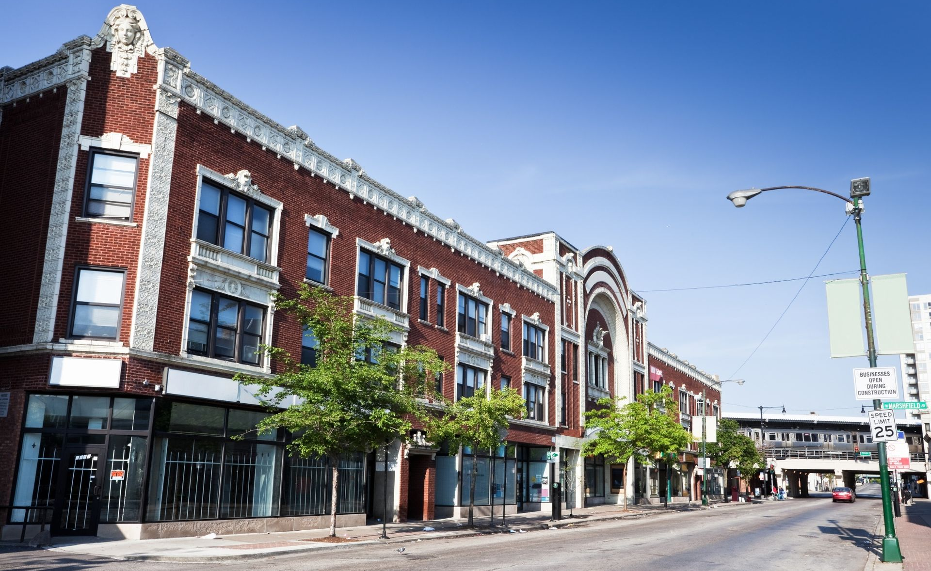 Downtown street with historic brick storefronts, awnings, and a few parked cars on a sunny day