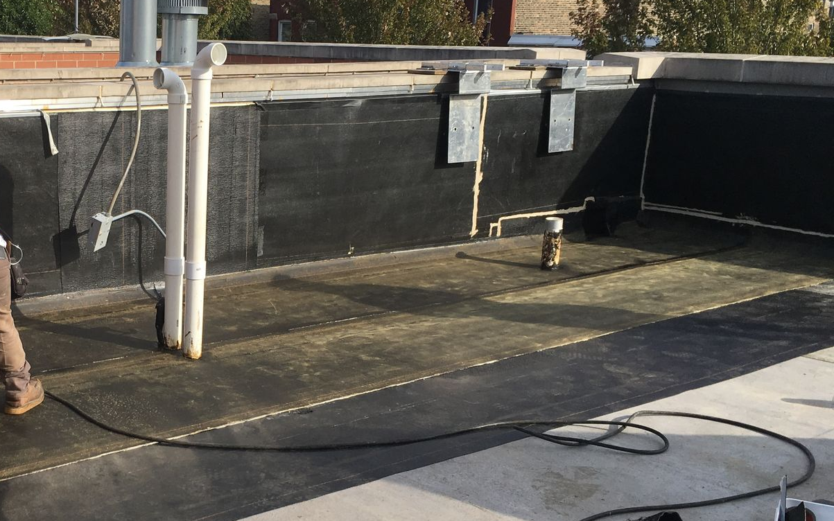 Rooftop with black waterproofing, white pipes, and a coiled cable