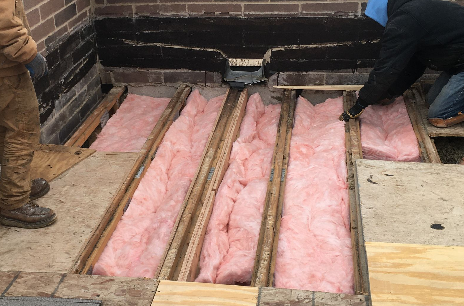 Pink insulation batts laid between floor trusses in a brick foundation