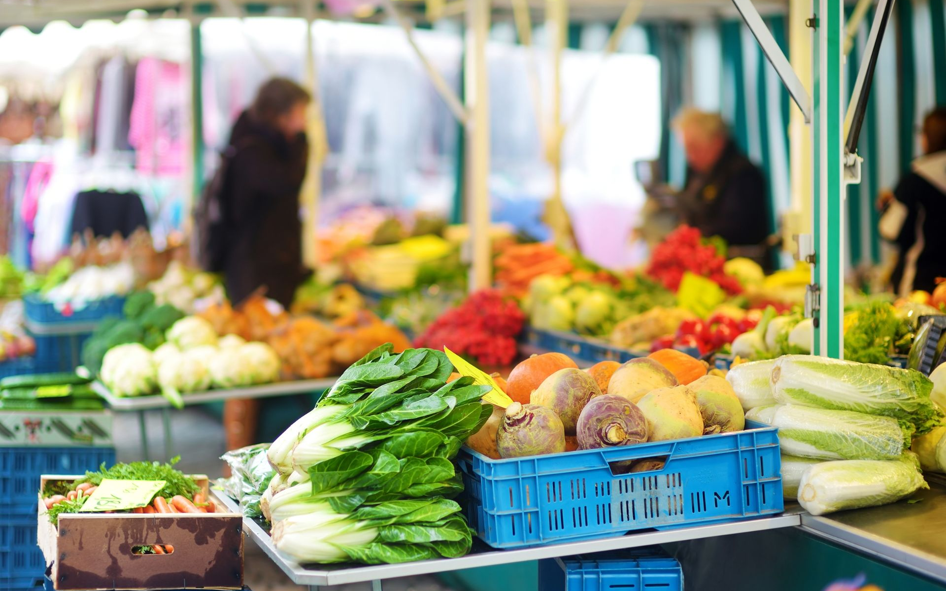 Outdoor farmer's market stalls with fresh vegetables and fruit in crates, shoppers