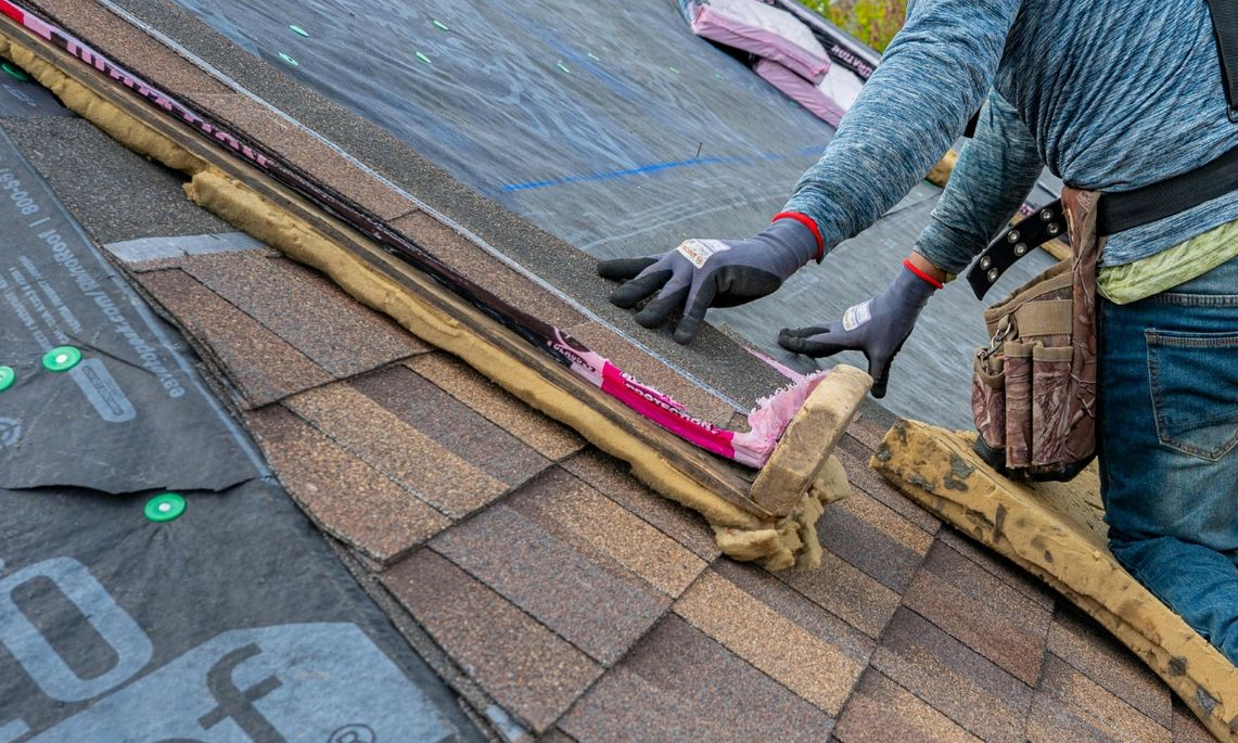 Workers installing roof underlayment and shingles on a sloped roof
