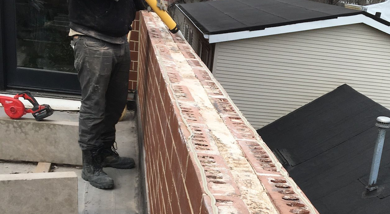 Worker applying caulk on a rooftop parapet wall