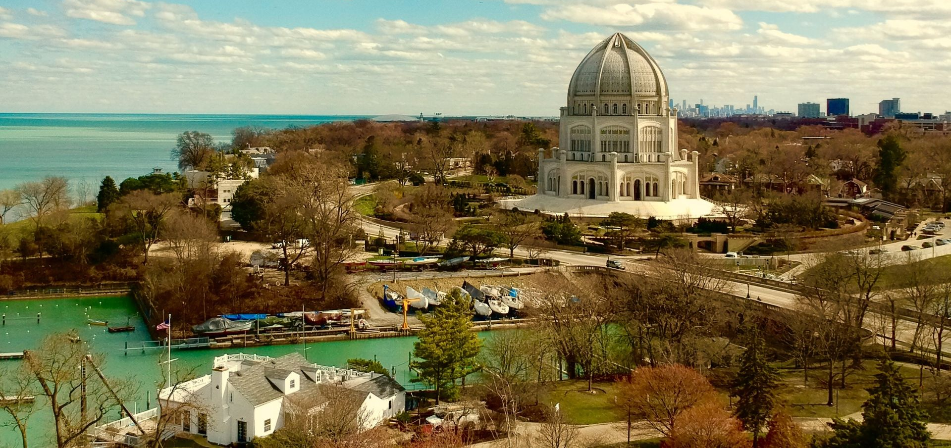 White domed waterfront temple(Bahai Temple) amid trees and boats with a bay