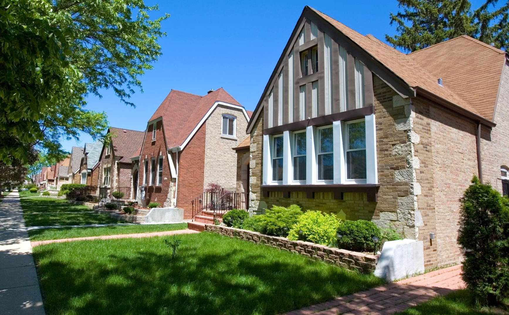 Row of brick townhouses with steep roofs along a tree-lined sidewalk
