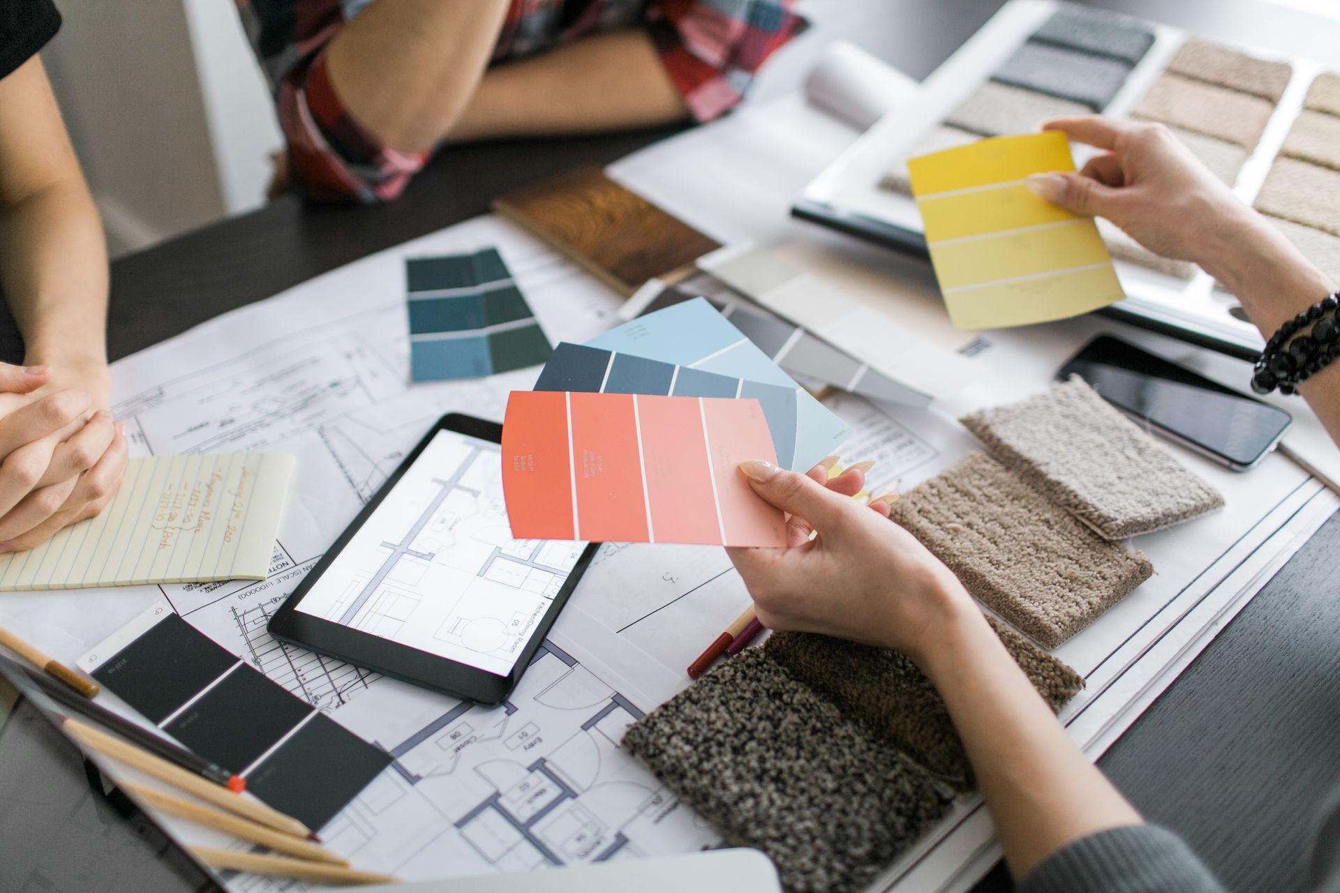 Interior decorators reviewing color swatches and fabric samples over design plans on a table.