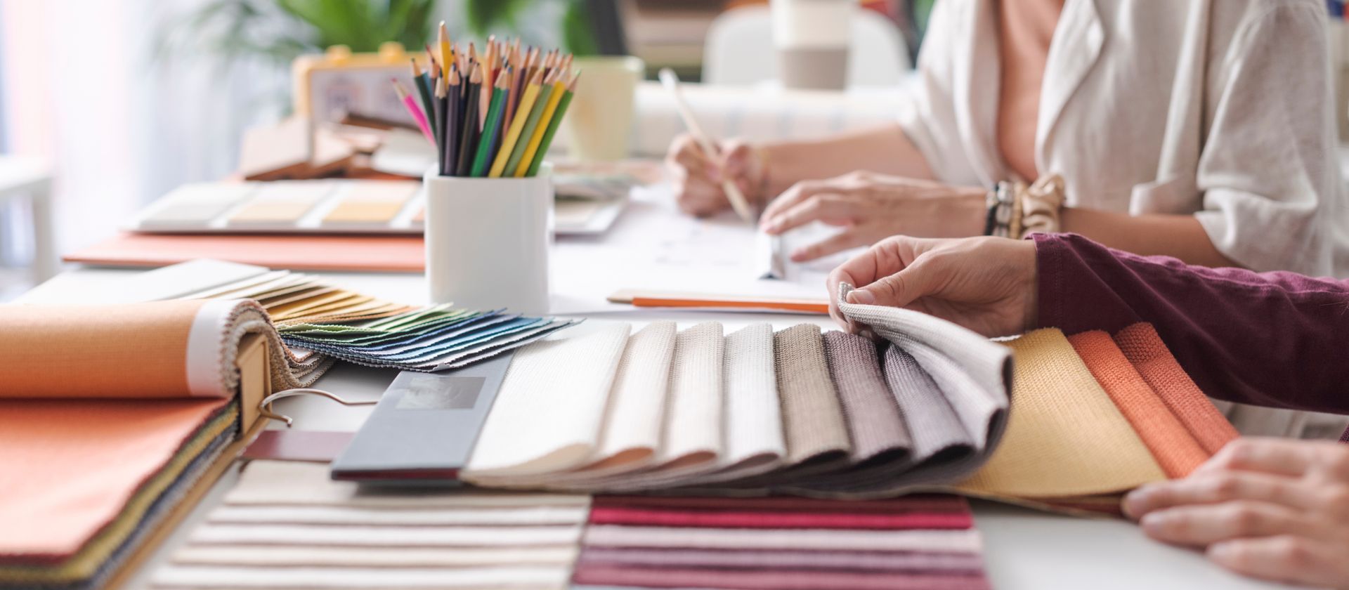 Interior decorators reviewing fabric swatches and color samples spread across a workspace. Interior decorators reviewing fabric swatches and color samples spread across a workspace.