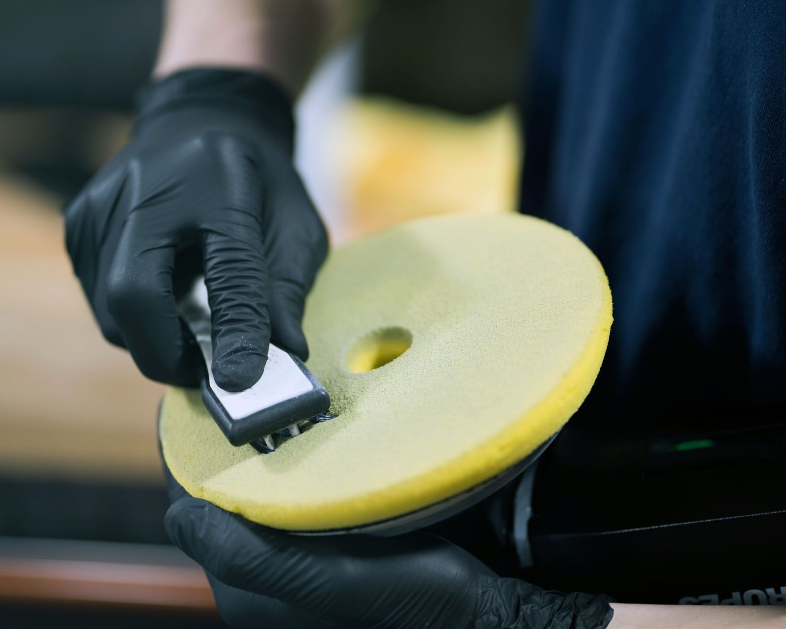 Gloved hands polishing a yellow foam pad with a black applicator tool