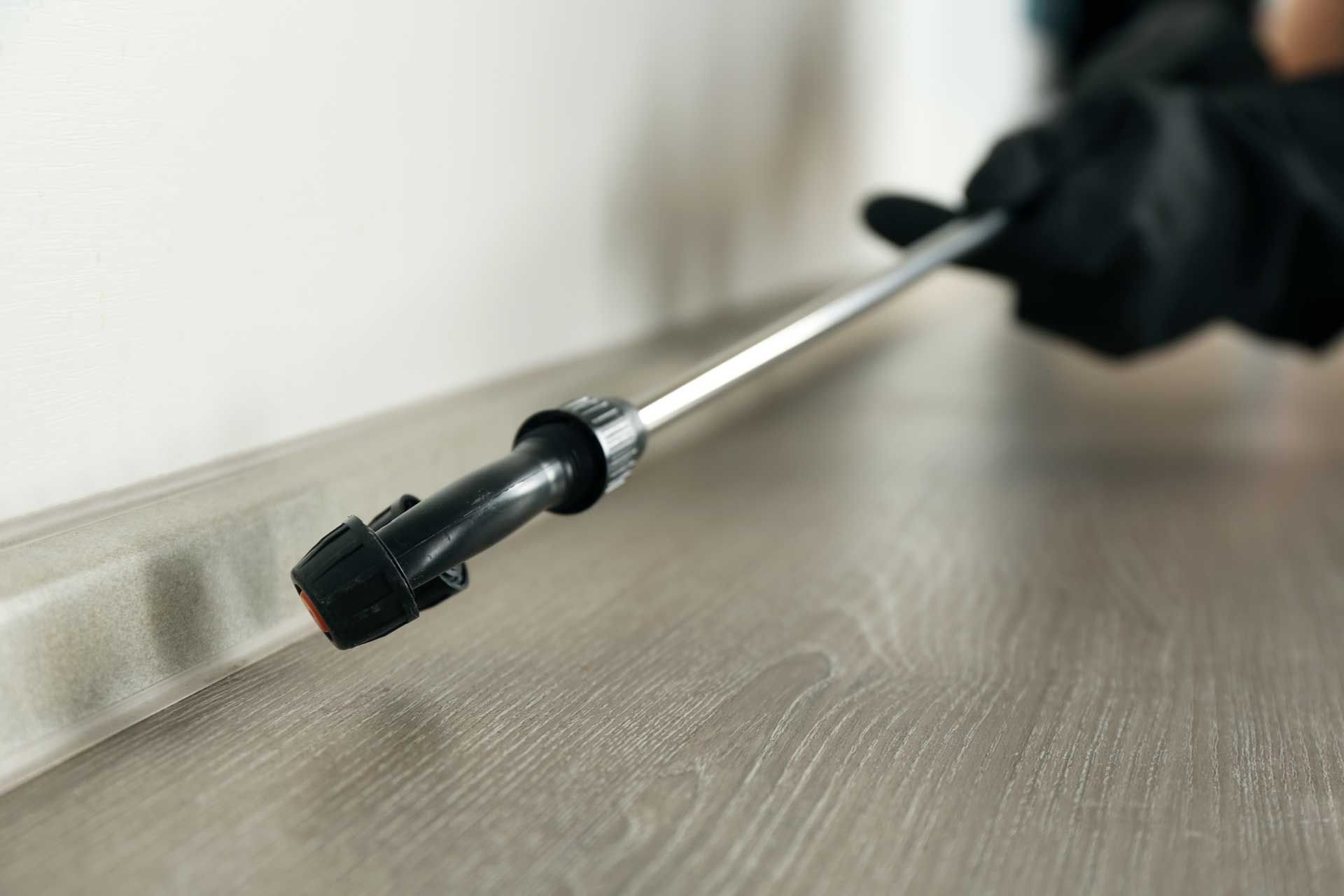 Gloved hand uses a metal tool with a black tip on a wood surface