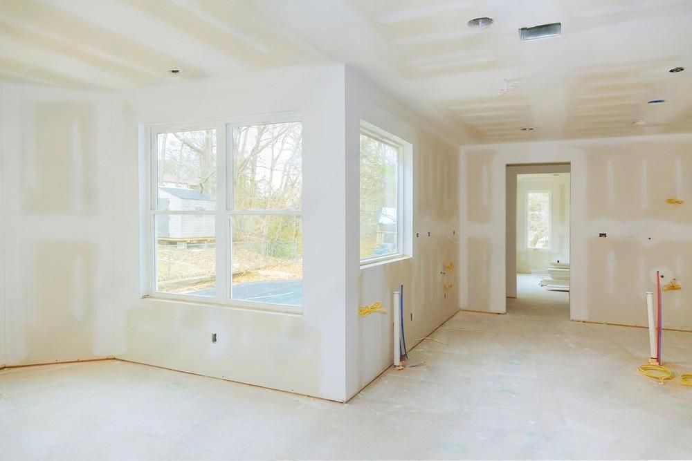 A room in a house under construction with drywall and windows.