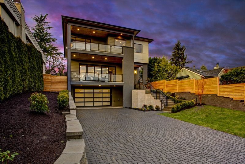 A large modern house with a brick driveway and a wooden fence.