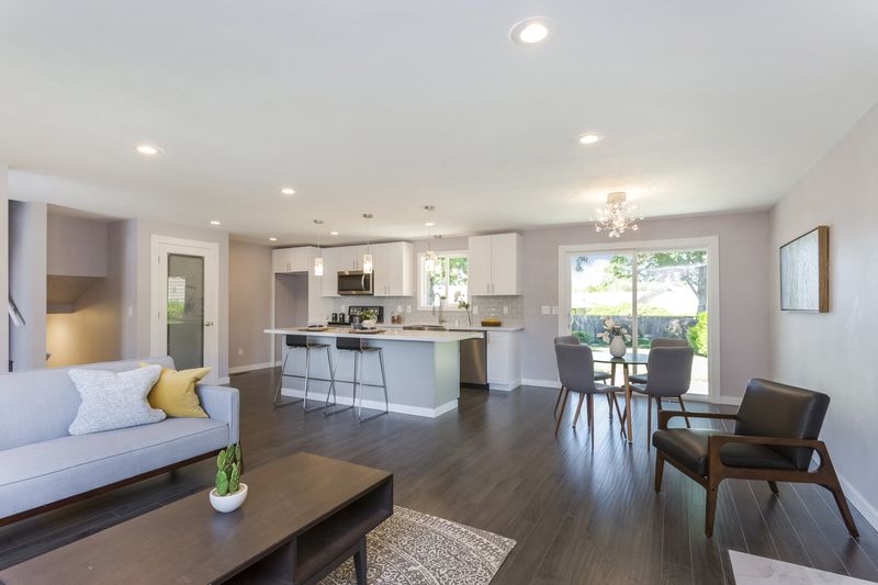 A living room with a couch , chairs , a table and a kitchen.