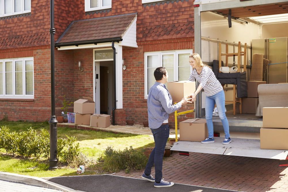 A Man And A Woman Are Loading Boxes Into A Moving Truck — Newcastle Moving & Storage in Cardiff, NSW