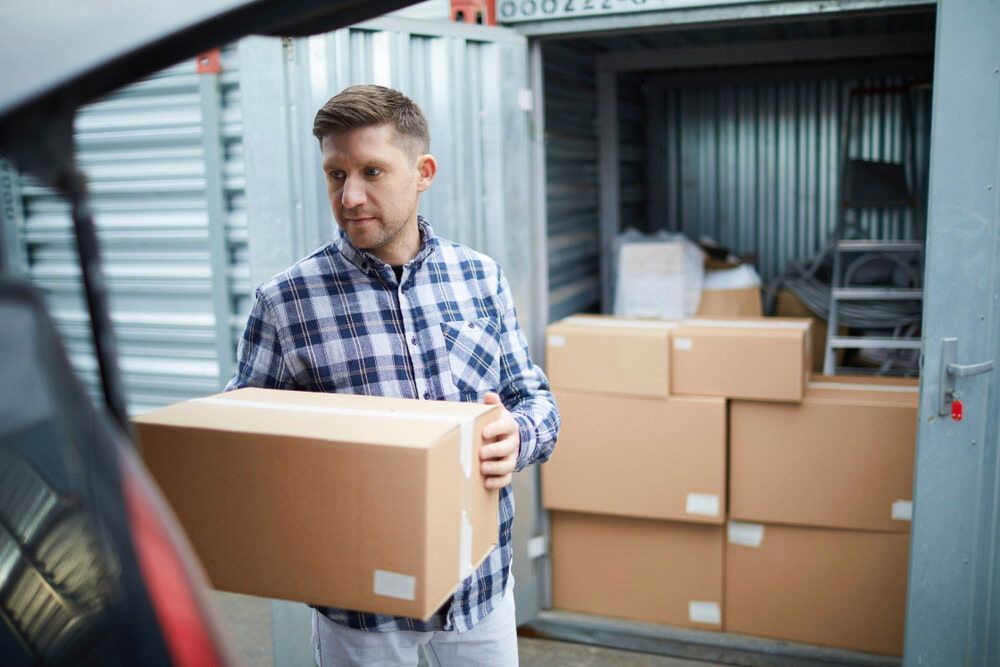 A Man Is Carrying A Cardboard Box Into A Storage Unit — Newcastle Moving & Storage in Salt Ash, NSW