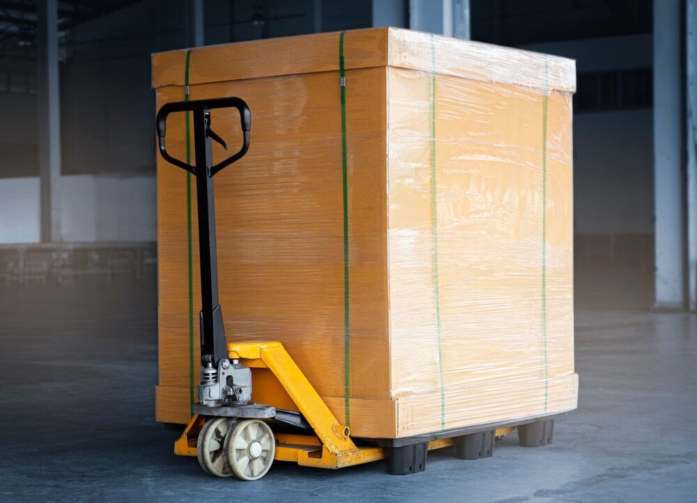 A Pallet Truck Is Carrying A Large Wooden Box In A Warehouse — Newcastle Moving & Storage in Salt Ash, NSW