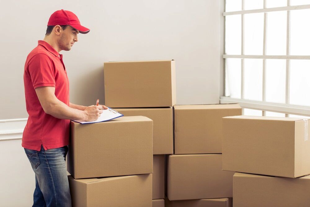 A Delivery Man Is Standing Next To A Pile Of Cardboard Boxes — Newcastle Moving & Storage in Belmont, NSW