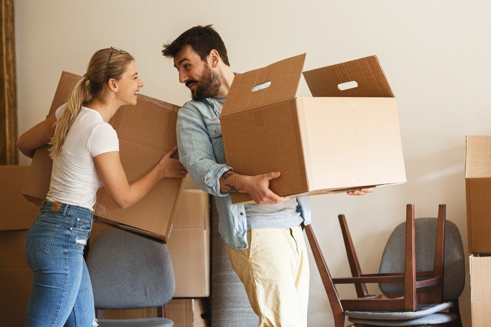 A Man And A Woman Are Carrying Cardboard Boxes Into A New Home — Newcastle Moving & Storage in Morisset, NSW