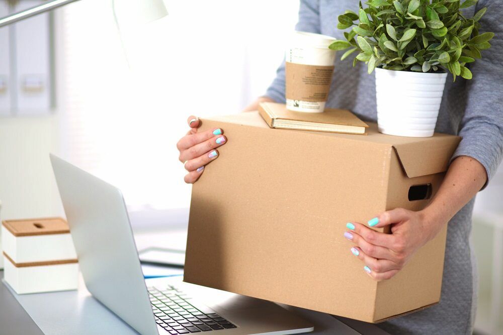 A Woman Is Holding A Cardboard Box In Front Of A Laptop — Newcastle Moving & Storage in Tuggerah, NSW