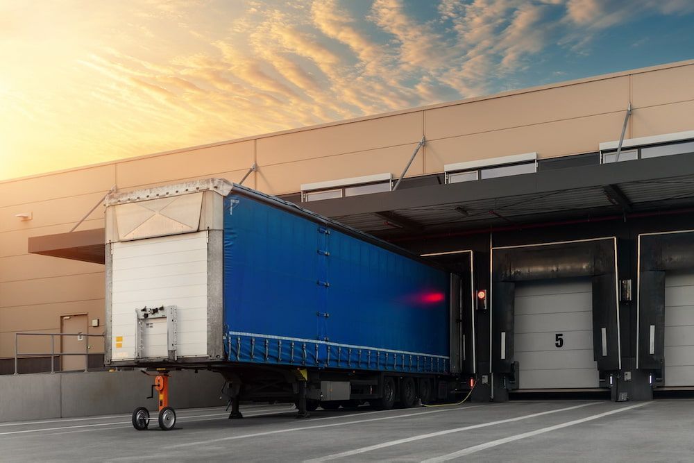 A Blue Semi Truck Is Docked At A Warehouse — Newcastle Moving & Storage in Warnervale, NSW