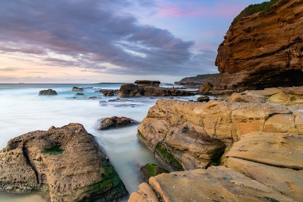 A Long Exposure Photo Of A Rocky Beach With A Cliff — Newcastle Moving & Storage in Swansea, NSW