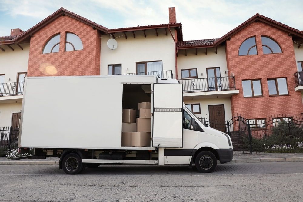 A White Moving Truck Is Parked In Front Of A Large House — Newcastle Moving & Storage in Woy Woy, NSW