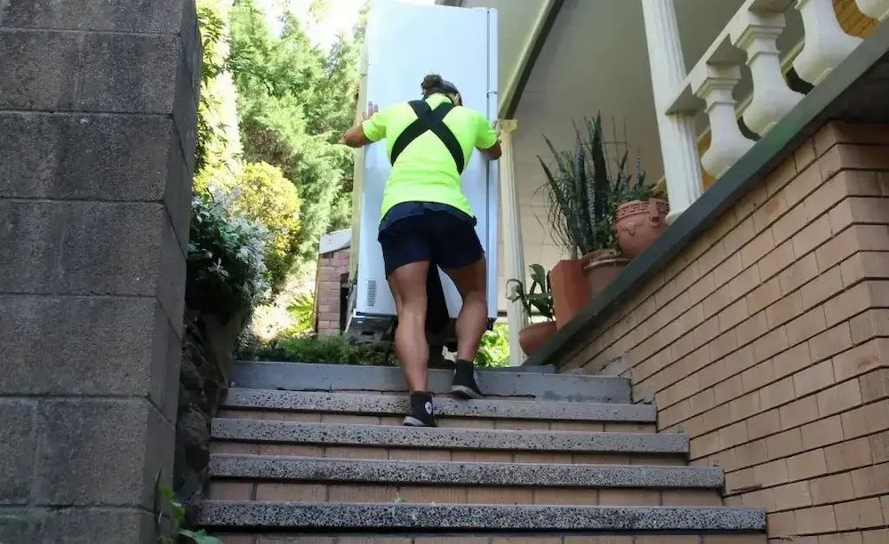 A Woman Is Carrying A Refrigerator Up A Set Of Stairs — Newcastle Moving & Storage in Salt Ash, NSW