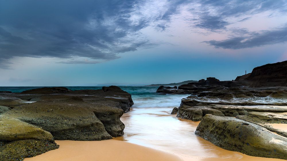 A Long Exposure Of A Beach With Rocks And Waves On A Cloudy Day — Newcastle Moving & Storage in Wyong, NSW