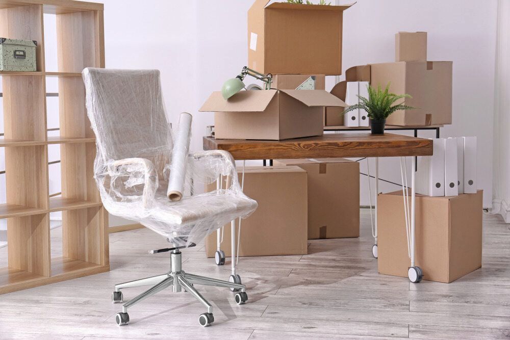 A Chair Is Wrapped In Plastic In An Office Surrounded By Cardboard Boxes — Newcastle Moving & Storage in Salt Ash, NSW