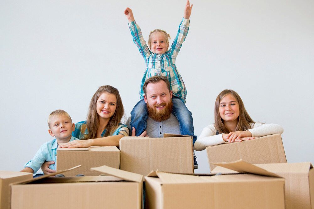 A Family Is Sitting In Cardboard Boxes In A New Home — Newcastle Moving & Storage in Newcastle, NSW
