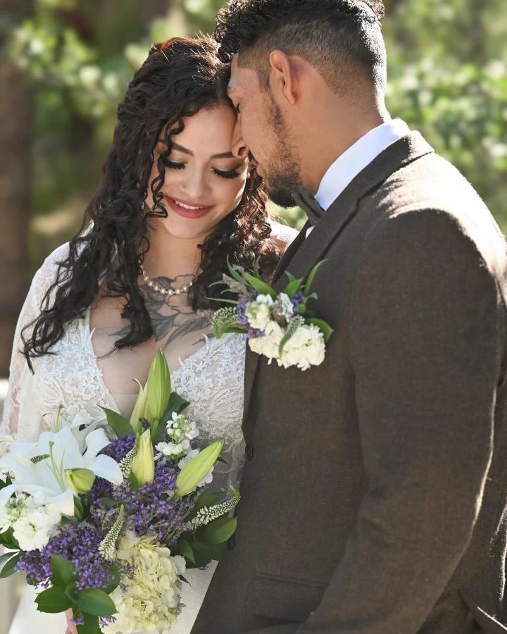 Bride and groom in formal attire sharing a close embrace with a white and purple bouquet outdoors