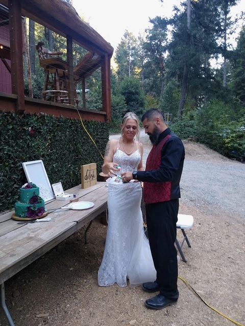 Bride and groom stand together outdoors beside a rustic wooden deck, sharing a moment at an event.