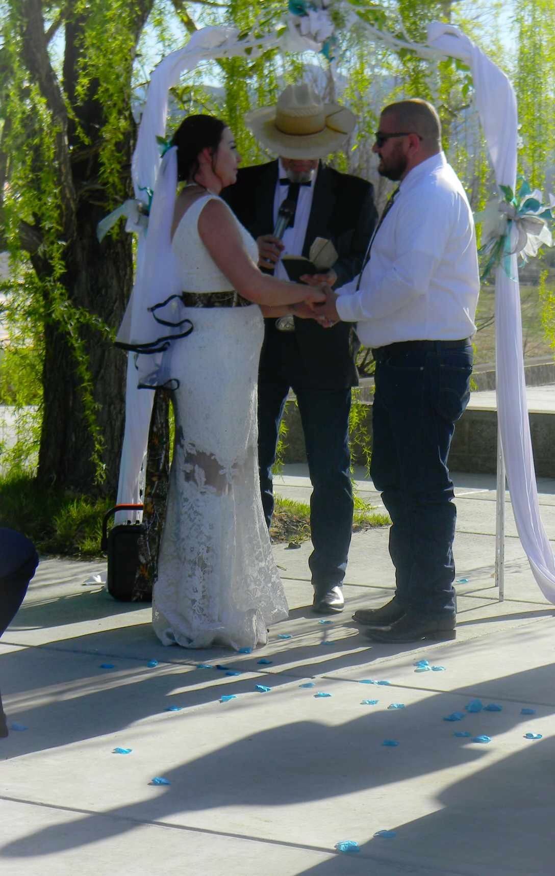 Outdoor wedding ceremony under a white arch, couple exchanging vows with officiant in a sunlit garden