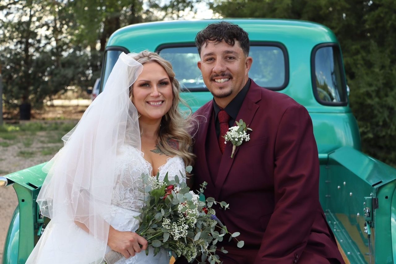 Bride and groom smiling in front of a vintage green truck, with bouquet and boutonniere