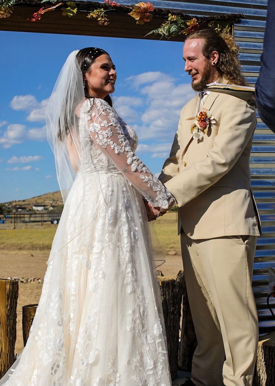 Bride and groom holding hands beneath a rustic arch at an outdoor wedding