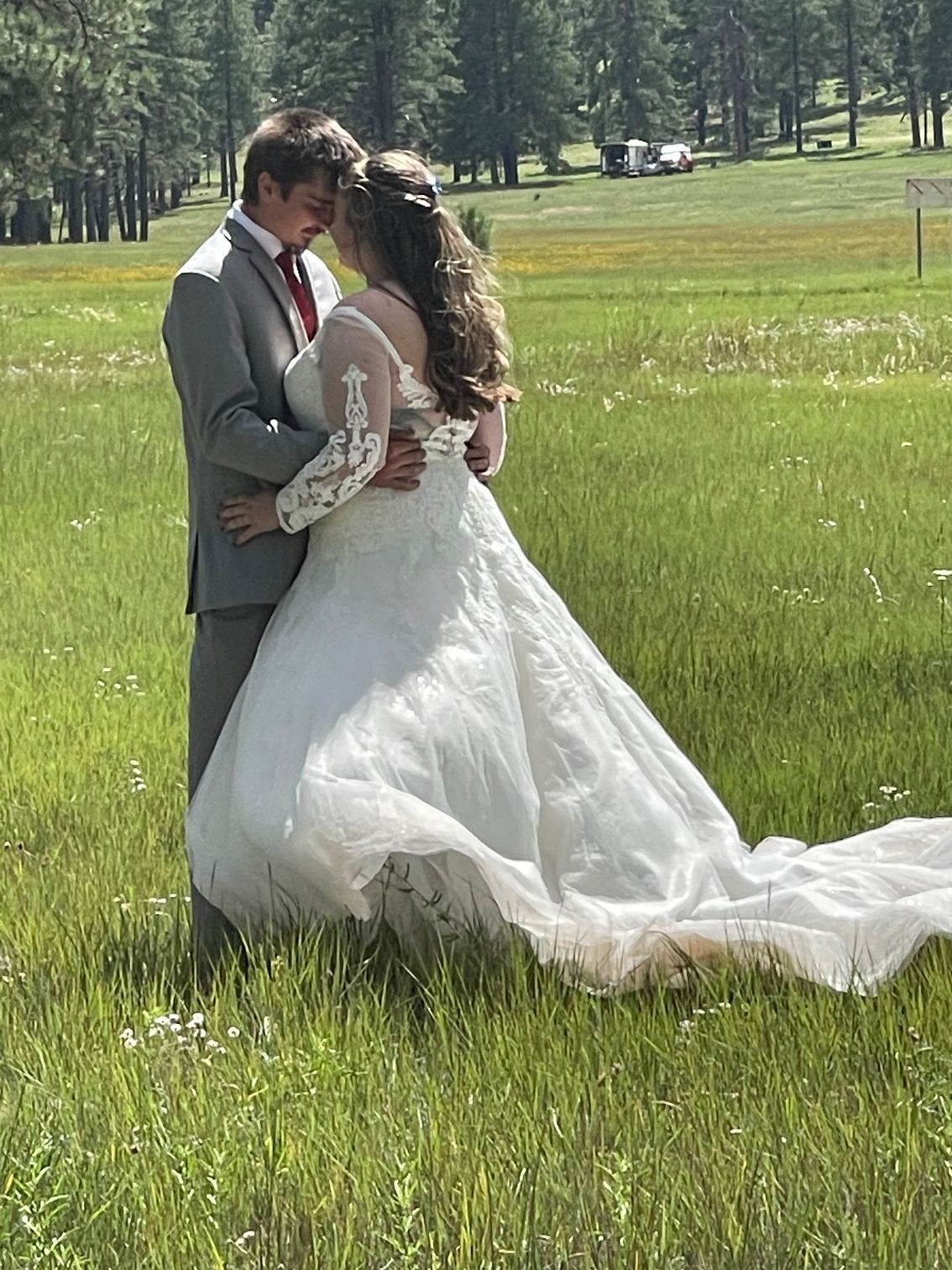 Bride and groom embracing in a white wedding dress on a sunny grassy field with trees