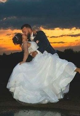 Bride and groom kissing as he lifts her, with a white gown at sunset