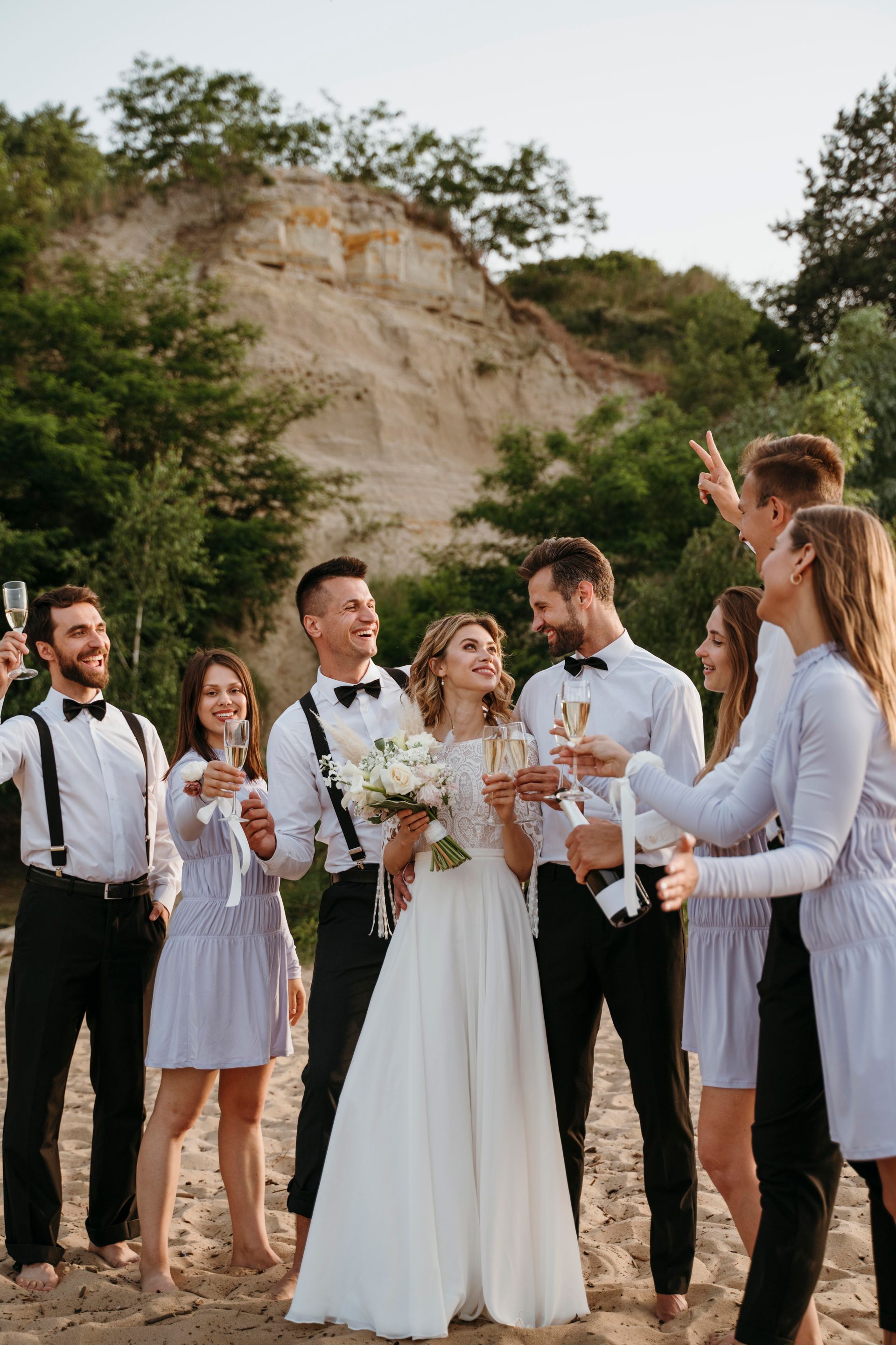 Wedding party on a beach clinking champagne glasses; bride and groom smiling, other guests cheering.