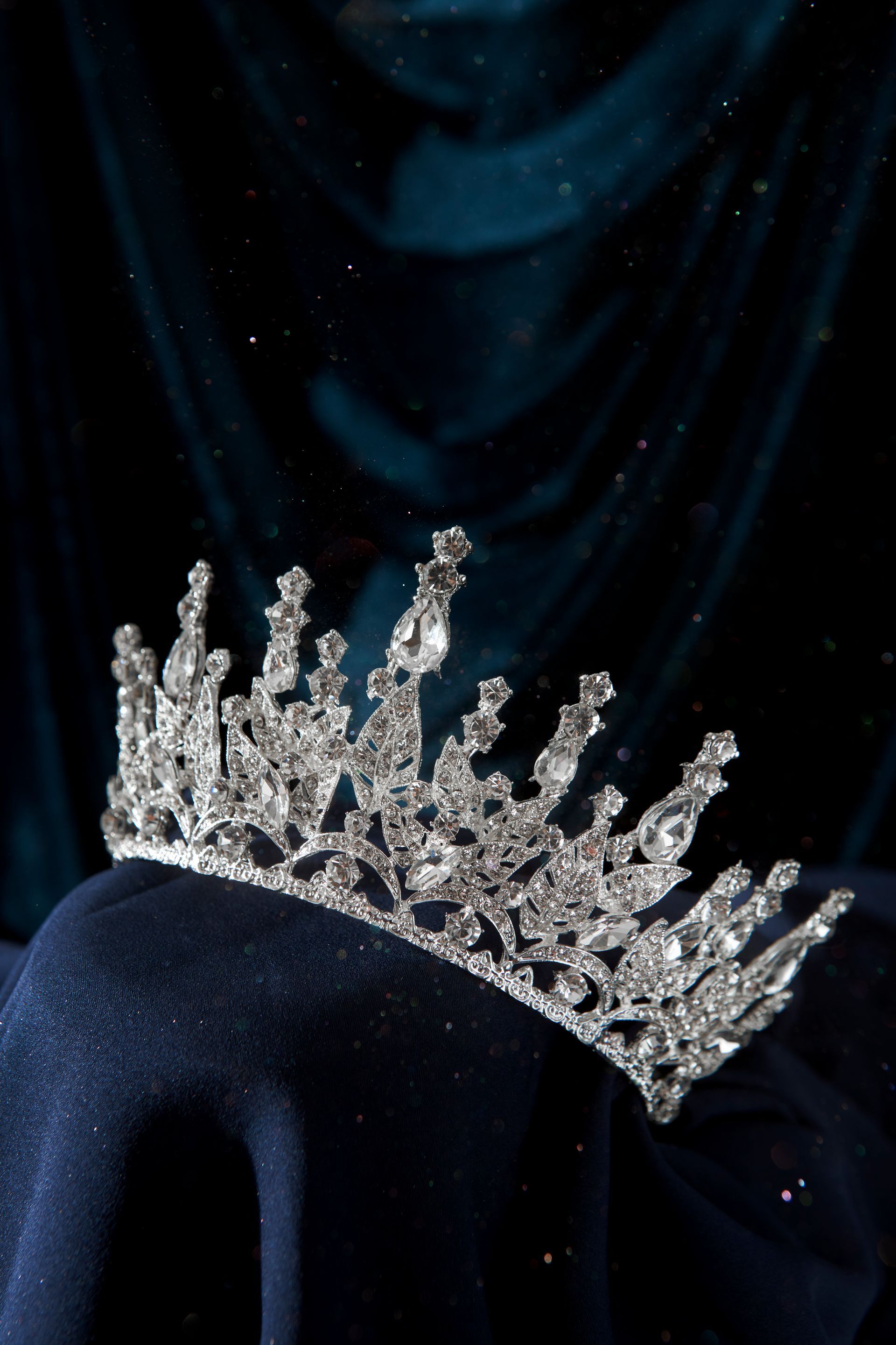 Silver tiara with clear crystals on dark blue velvet.