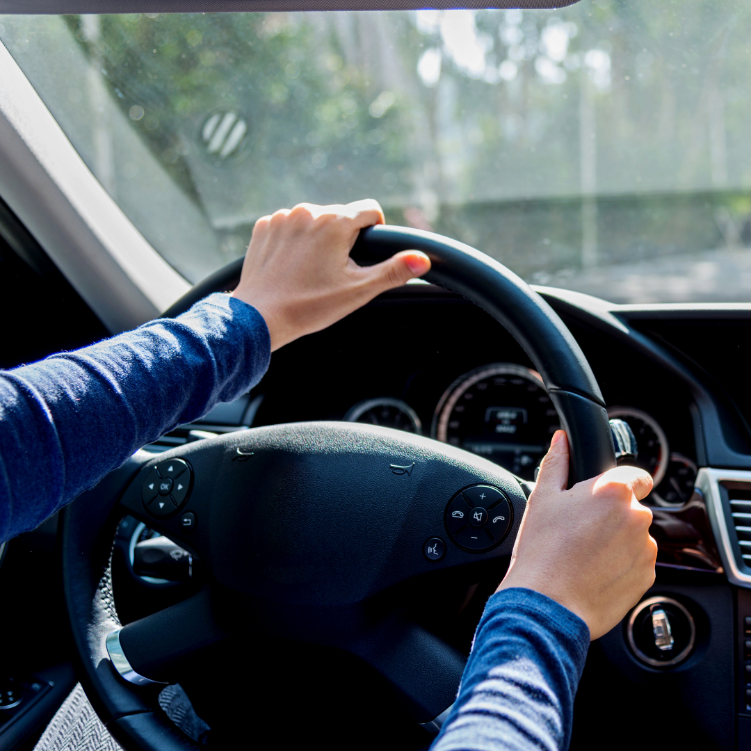Hands gripping a black steering wheel inside a car, driving.