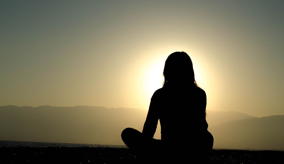 Silhouette of person meditating at sunset, mountains in background.