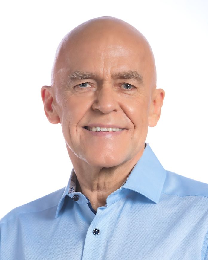 Bald man wearing a light blue button-down shirt smiles at the camera.