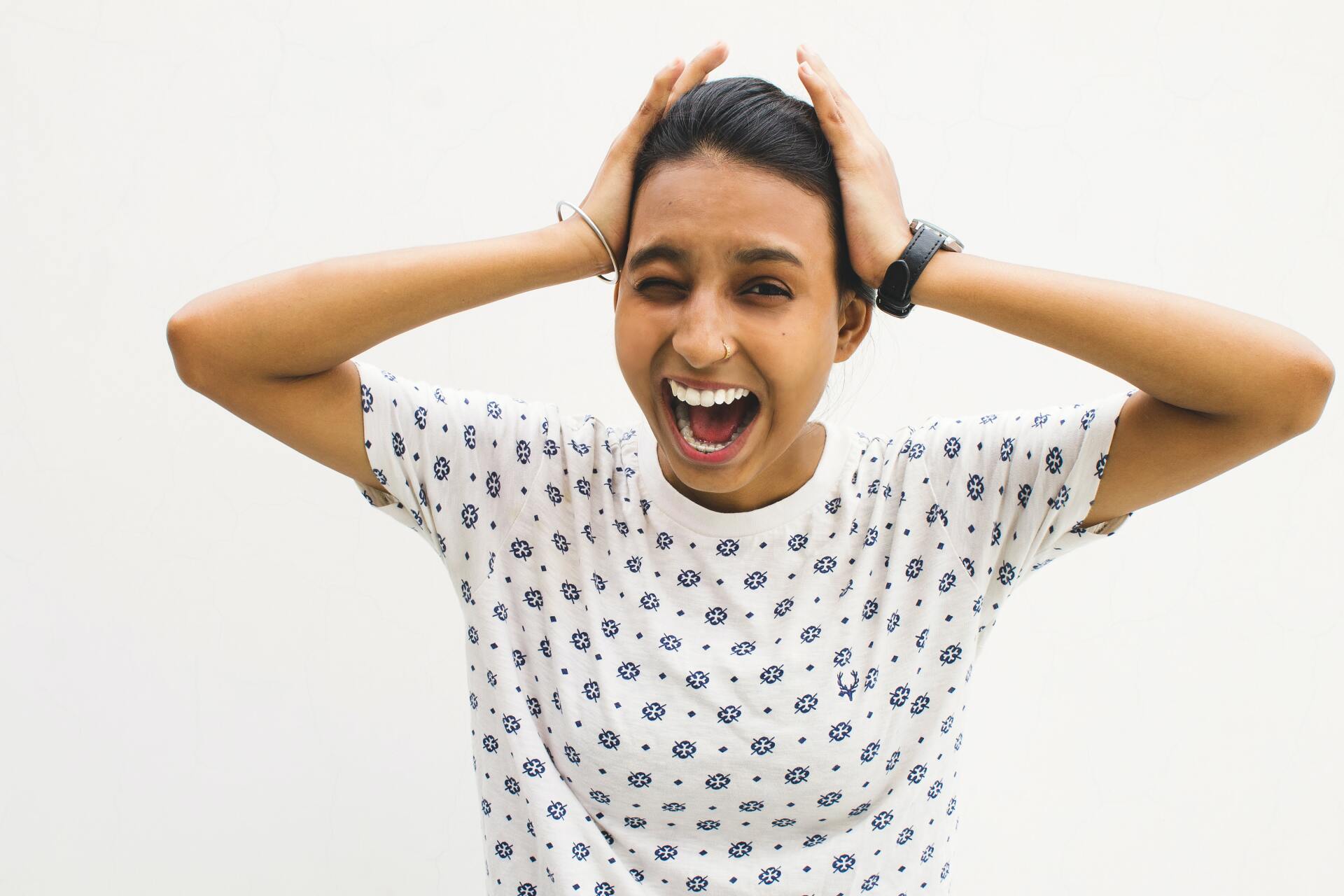 Person with hands on head, mouth open, shouting in front of a white background.