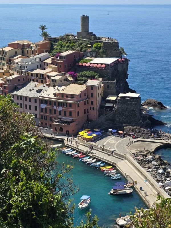Coastal Italian village with colorful buildings, harbor, boats, and a tower on a cliff.