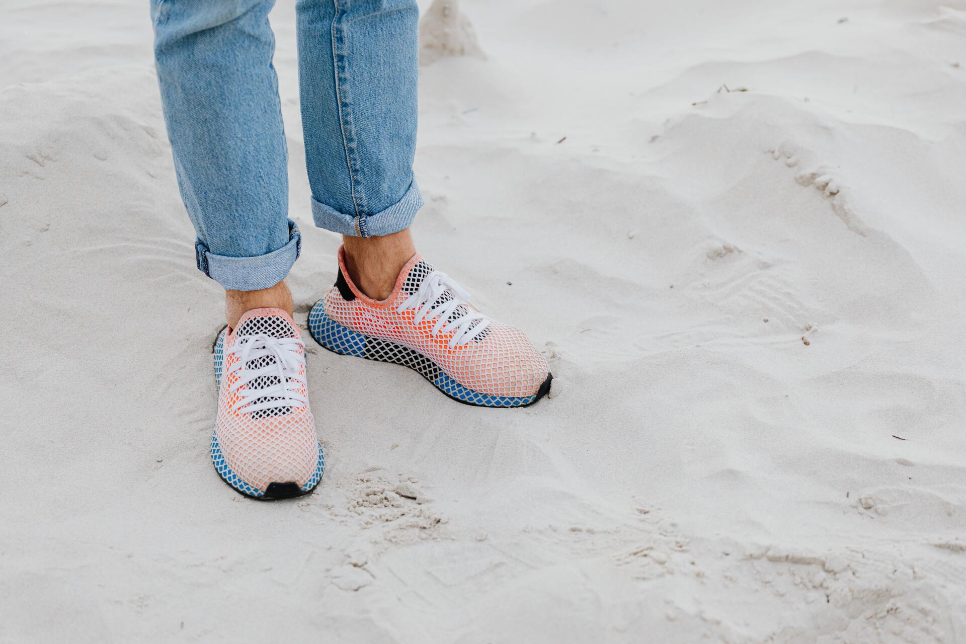 Person wearing light-wash jeans and colorful sneakers standing on white sand.