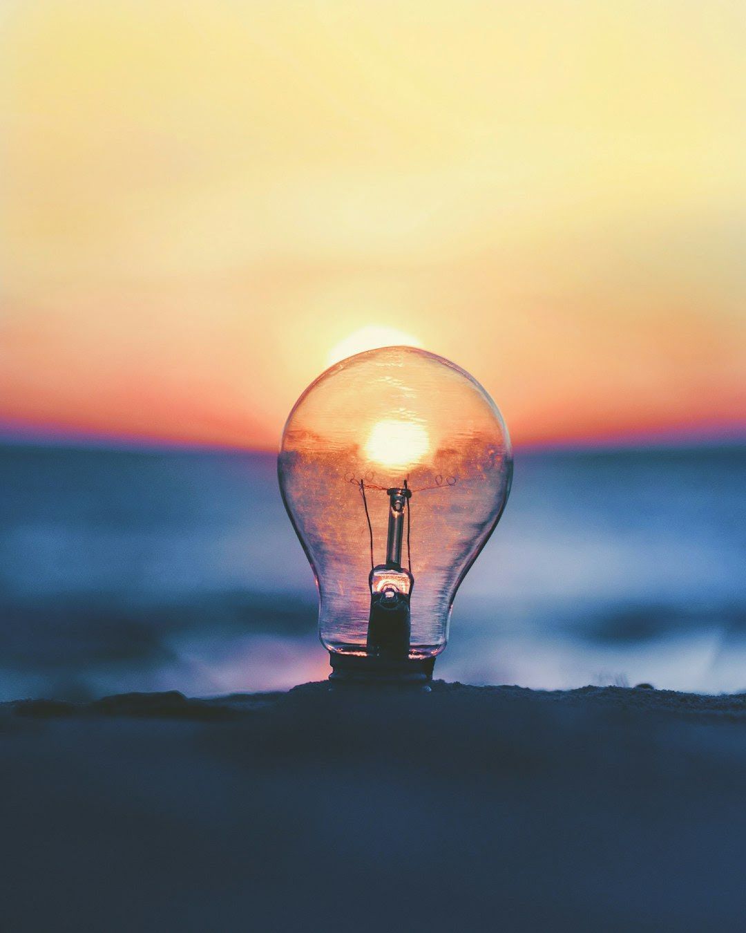 Lightbulb with the sunset inside, silhouetted on a beach.